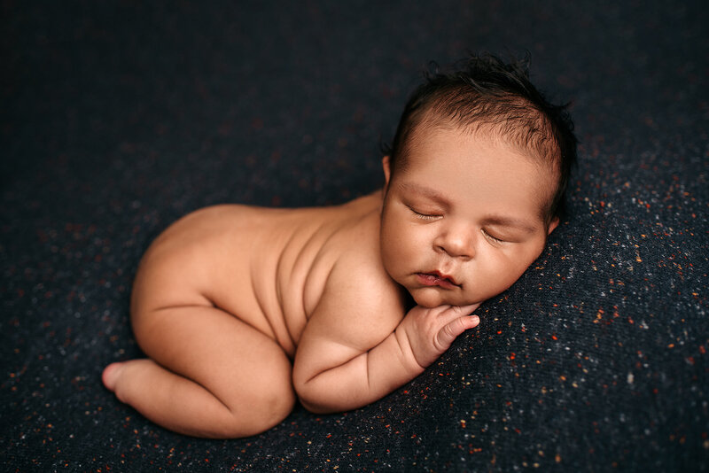 Baby boy lying on blue speckled backdrop in booty up pose in Jacksonville, FL.