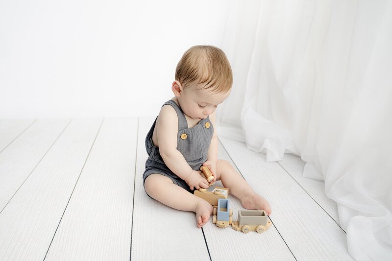 7 month old plays with wooden toys dresssed in blue overalls
