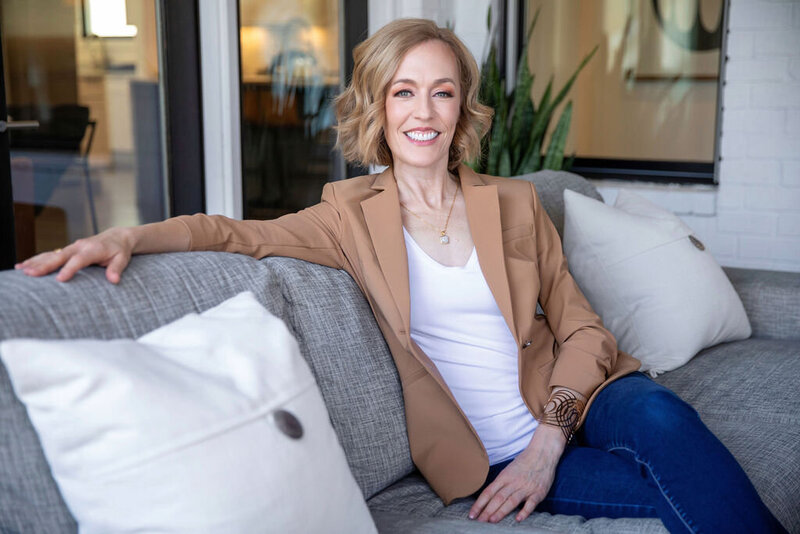 Heather Ebert, writer and intuitive coach, lounges on a gray couch.