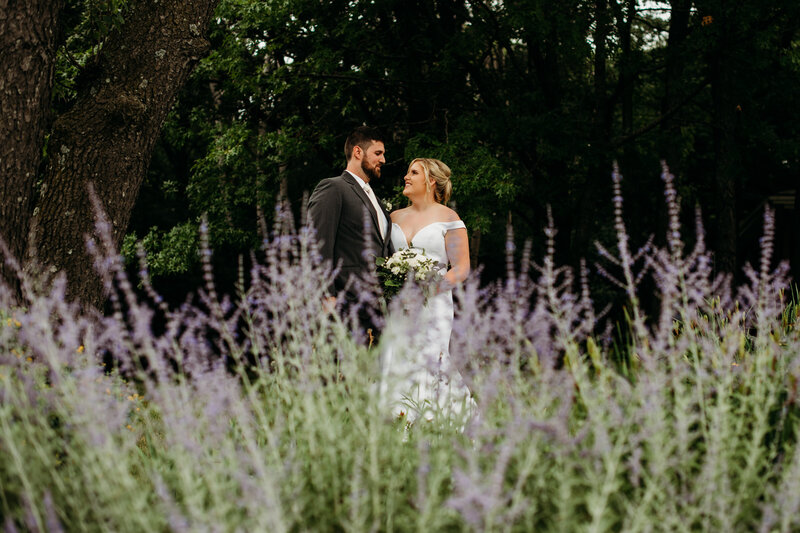 Bride and groom smiling at each other with lavender in front of them