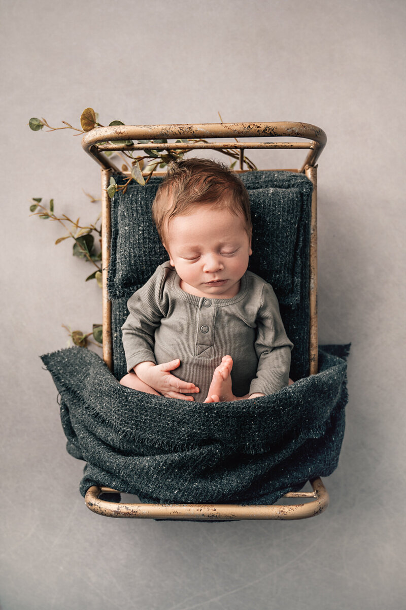 baby boy laying on little bronze bed