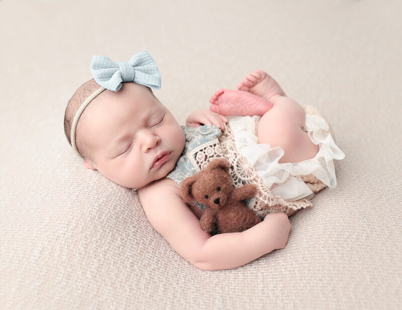 Newborn girl holding a teddy bear in a studio setting, showcasing professional photography in Rochester, NY.