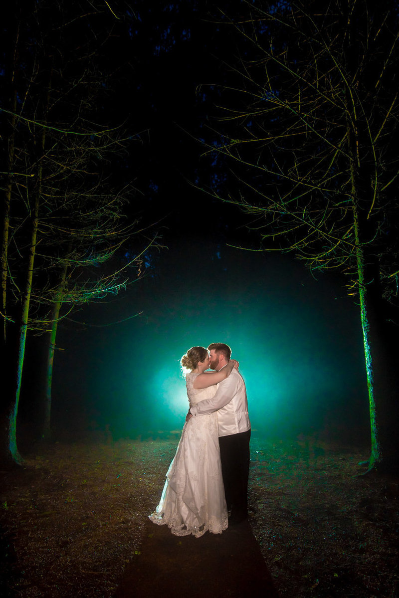 A turqouise backlit photo of a bride and groom kissing