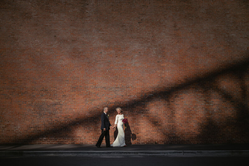 A bride and groom holding hands and walking in front of a red brick building.