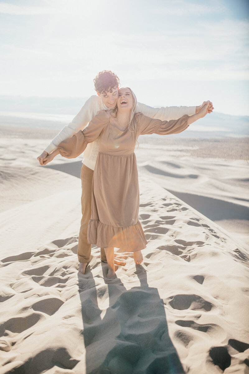 Engaged couple embrace on sand dunes