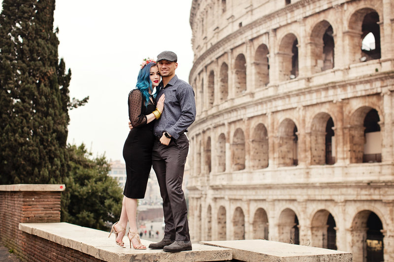 A newly engaged couple on the ledge in front of the Colosseum. Taken by Rome Photographer, Tricia Anne Photography.
