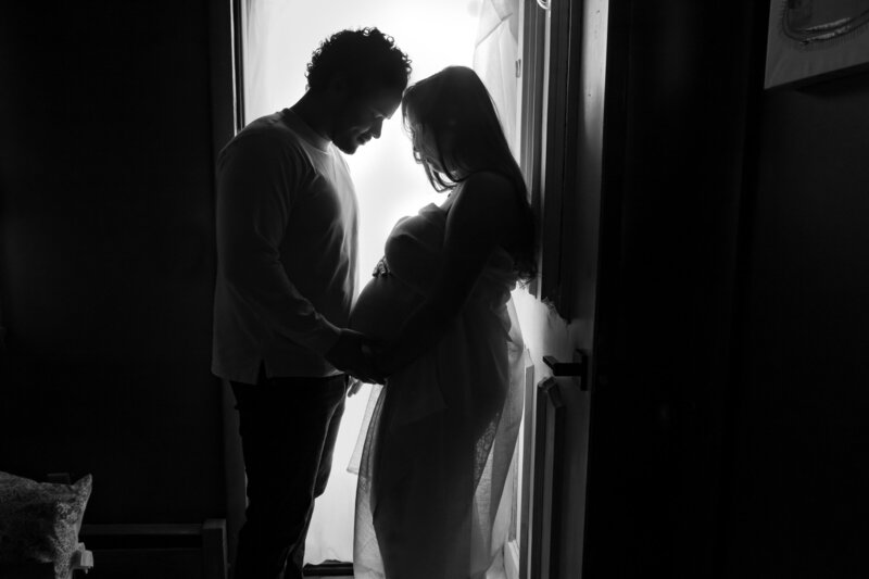 A black and white photo of a couple standing close together holding a pregnant stomach.