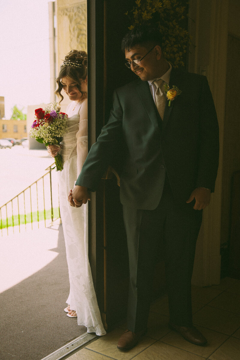 The mother of the bride prepares the veil for the bride as the sun shines through a window, offering a beautiful backlight effect