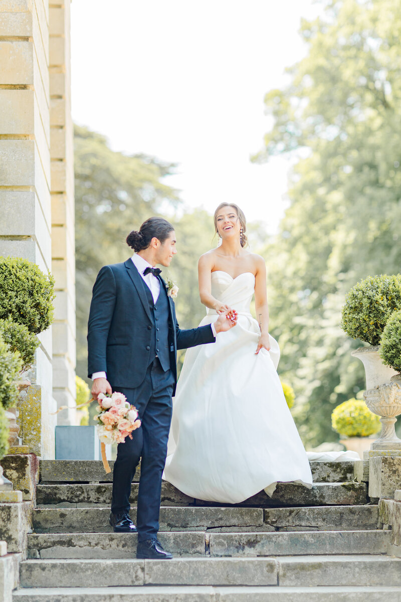 Bride and groom walk down stone steps at their Paris destination wedding. The groom is leading the bride and they are looking and laughing at each other. Captured by US-based destination wedding photographer Liana Huot of Lia Rose Weddings