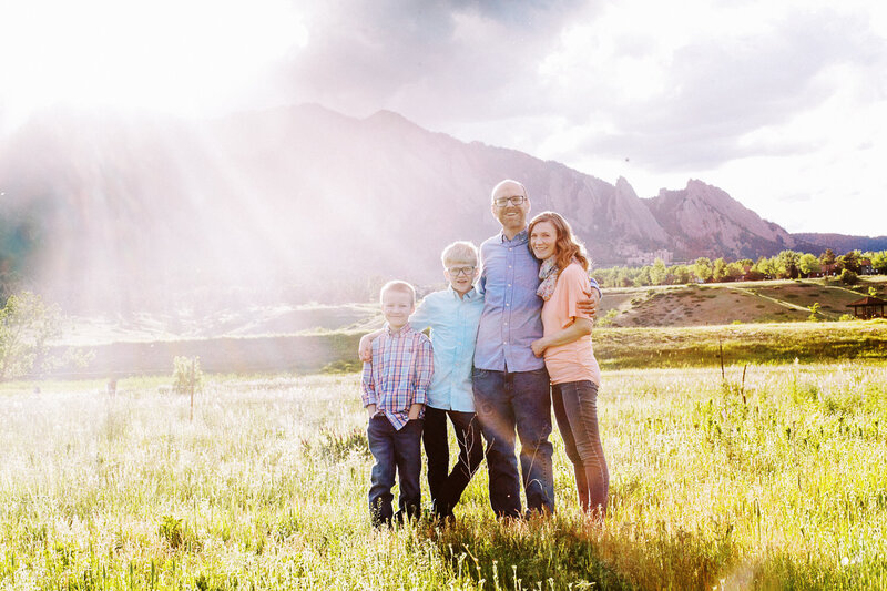 family stands in front of the boulder flatirons with sunflare