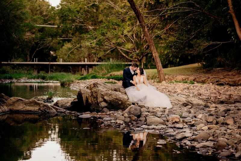 Bride and groom sitting along the river on a rock, affectionately staring at each other