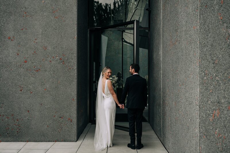a bride looks over her shoulder at the camera in front of an architecturally designed concrete wall at ravenscar house museum