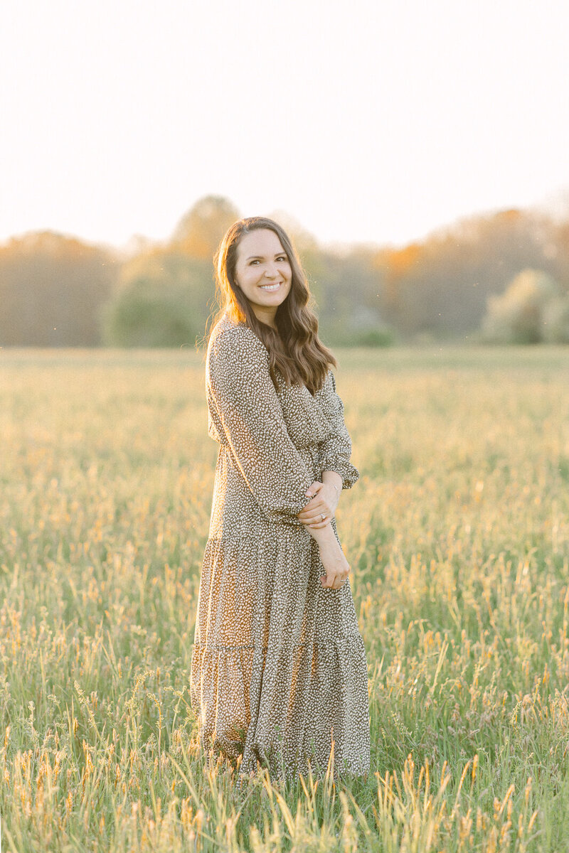 Corinne Isabelle, a Boston family photographer,  standing in a field during golden hour.
