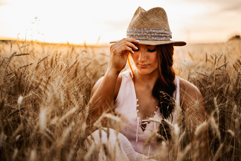 Girl holds hat and looks down in wheat field