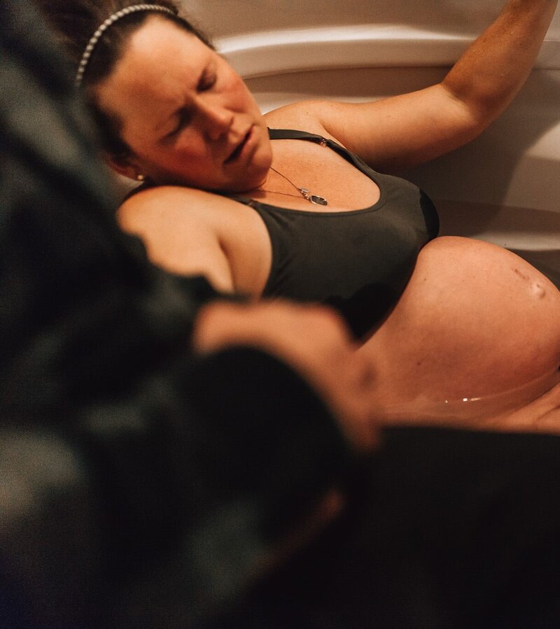 Woman laboring in a tub at a birthing center with partner doula and midwife supporting