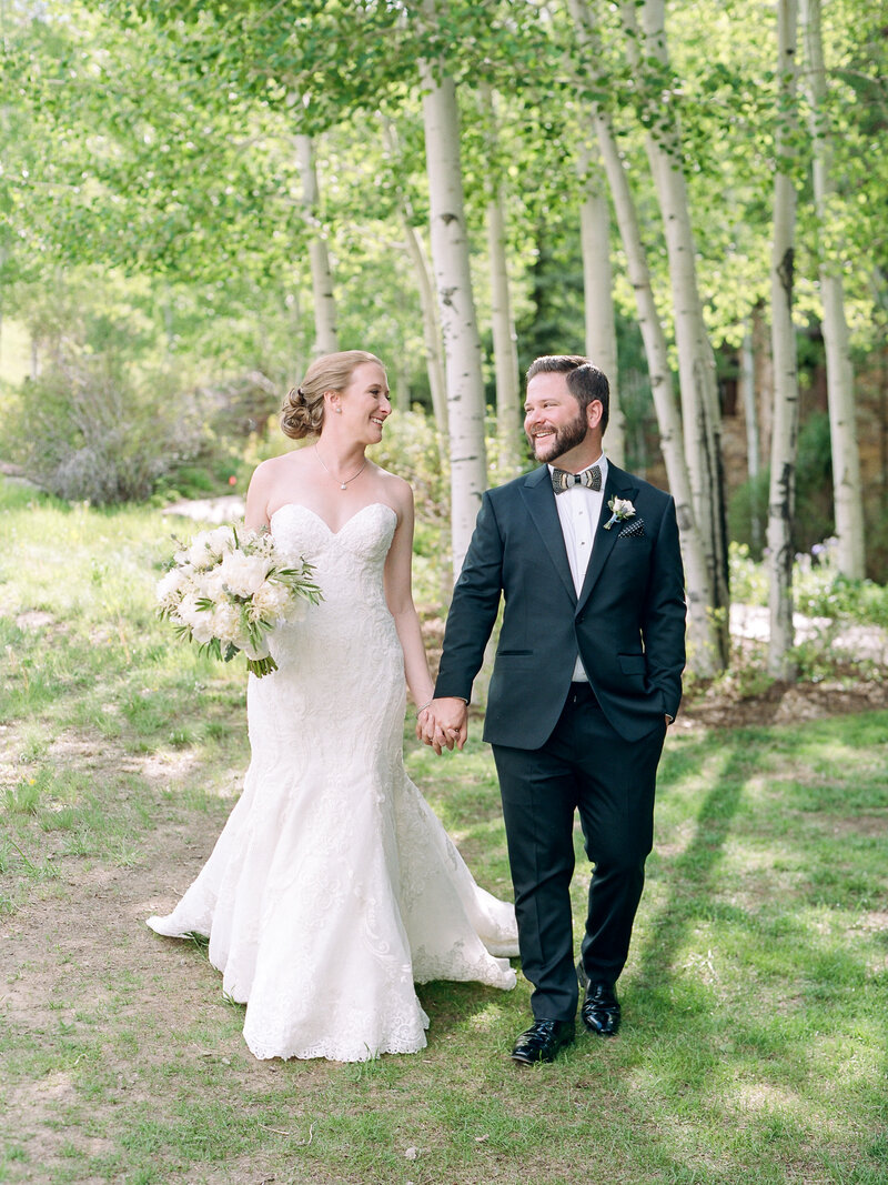 Testimonial photo of bride and groom holding large white bouquet, trees behind