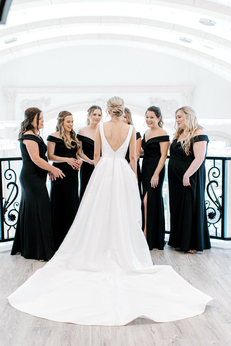 bride in wedding dress with long train standing with bridesmaids in black dresses