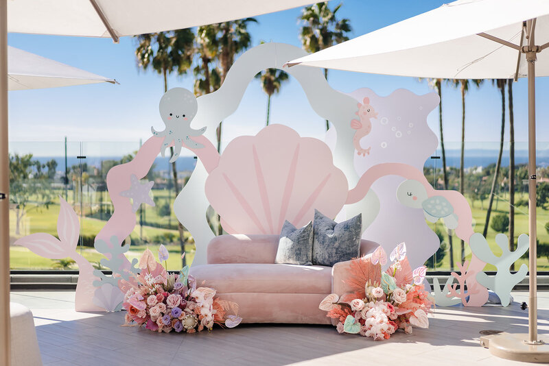 Outdoor baby shower with a cute underwater them. Image shows a pink coach with a clam shell, octopus, starfish, and other aquatic animal cutouts surrounding it.