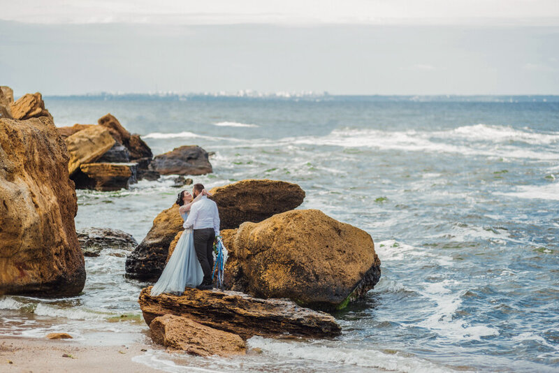 bride and groom standing on rocks in ocean