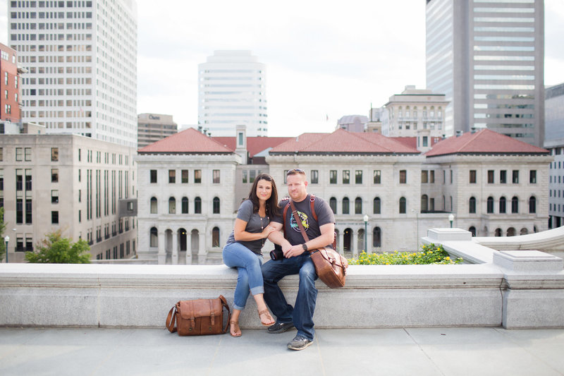 A couple sitting on a stone ledge with urban buildings in the background, captured by D.C. Wedding Photographers.