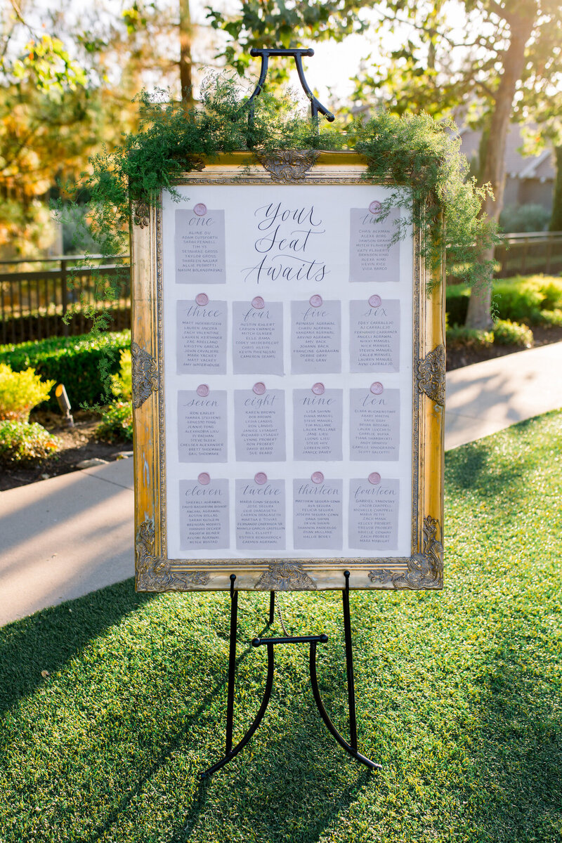 Seating chart with handmade paper cards, calligraphy, and wax seals inside a gold frame