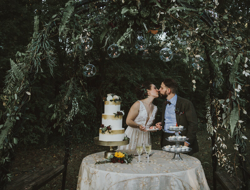 bride and groom kissing next to wedding cake