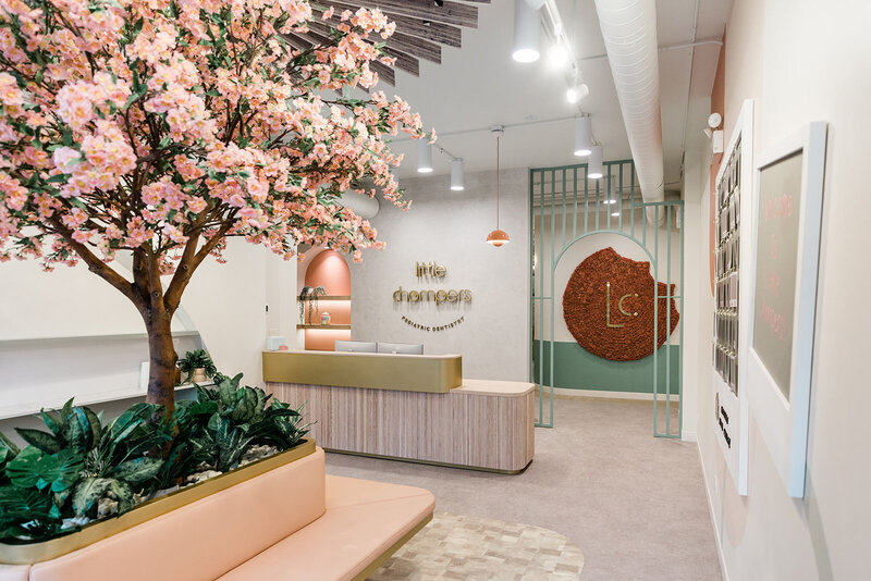 Little Chompers Pediatric Dentistry is the best pediatric dentist near me! Pictured is a view of their beautiful, mid-century modern style reception area, featuring natural textures and peachy pink florals to put young patients and parents at ease.