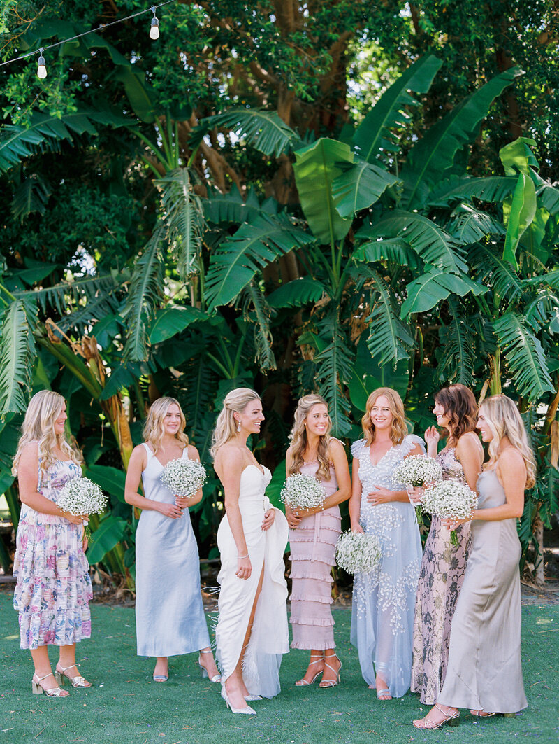 la quinta resort and spa wedding getting ready moment with seven bridesmaids and bride with white babies breath bouquets. Bridesmaids with mismatched bridesmaids dresses under palm trees.