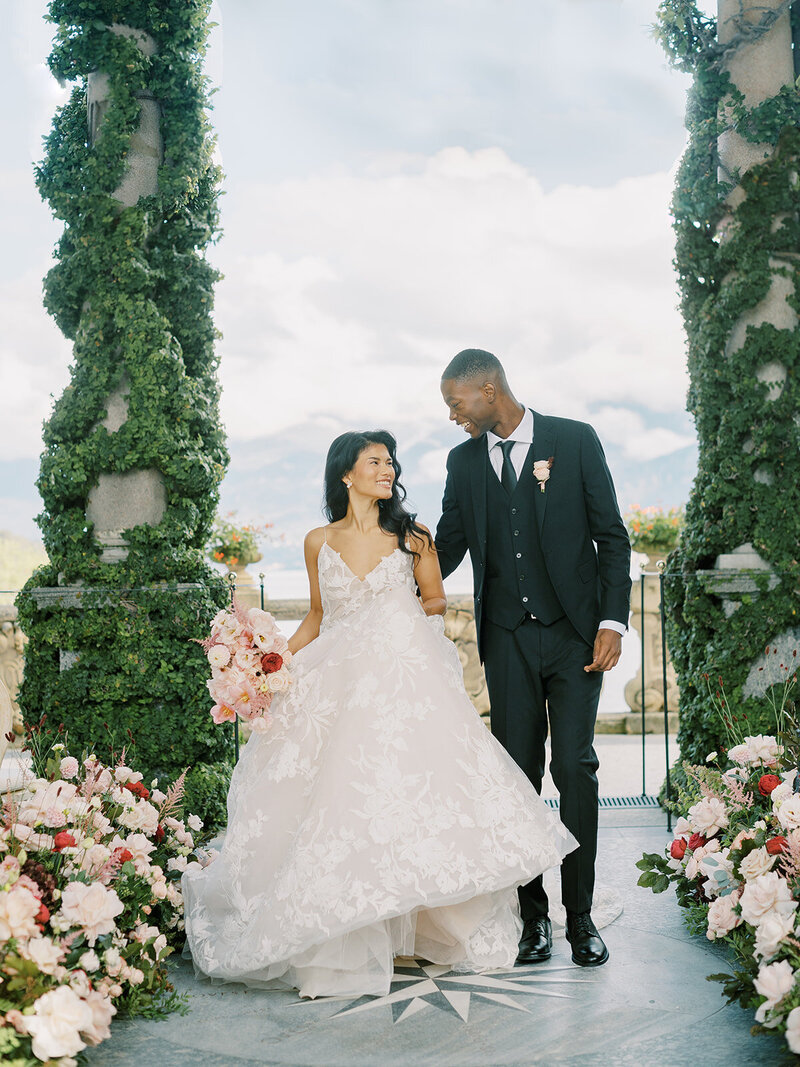 A-bride-and-groom-standing-in-front-of-an-archway-with-flowers