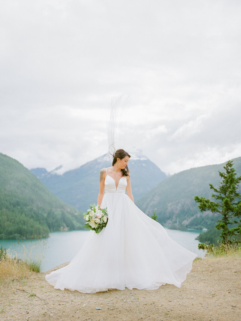 bride looking down over her shoulder as her veil is being swift up by the wind at Diablo Lake in Washington