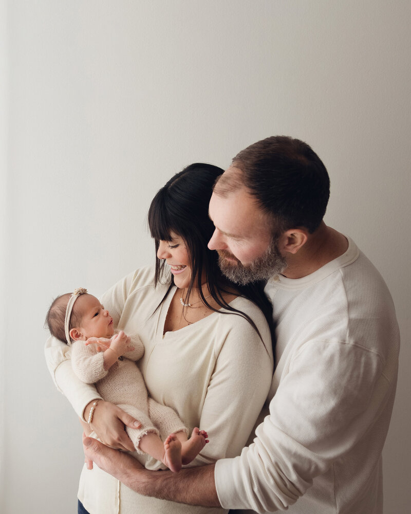 Smiling parents looking at newborn baby in white clothing