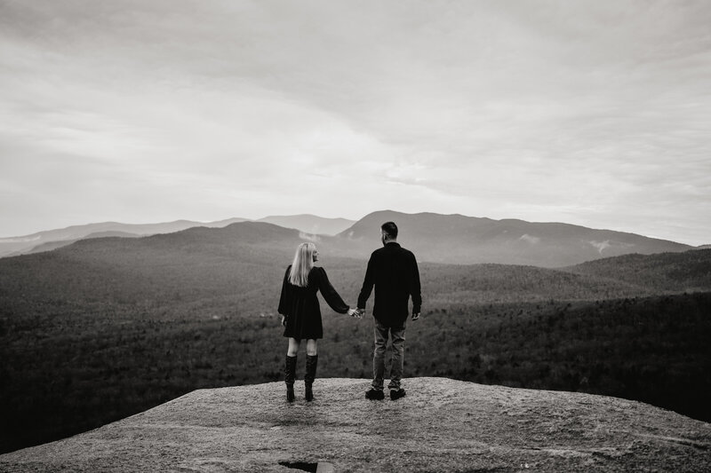 Couple at top of mountain holding hands looking out at view in NH