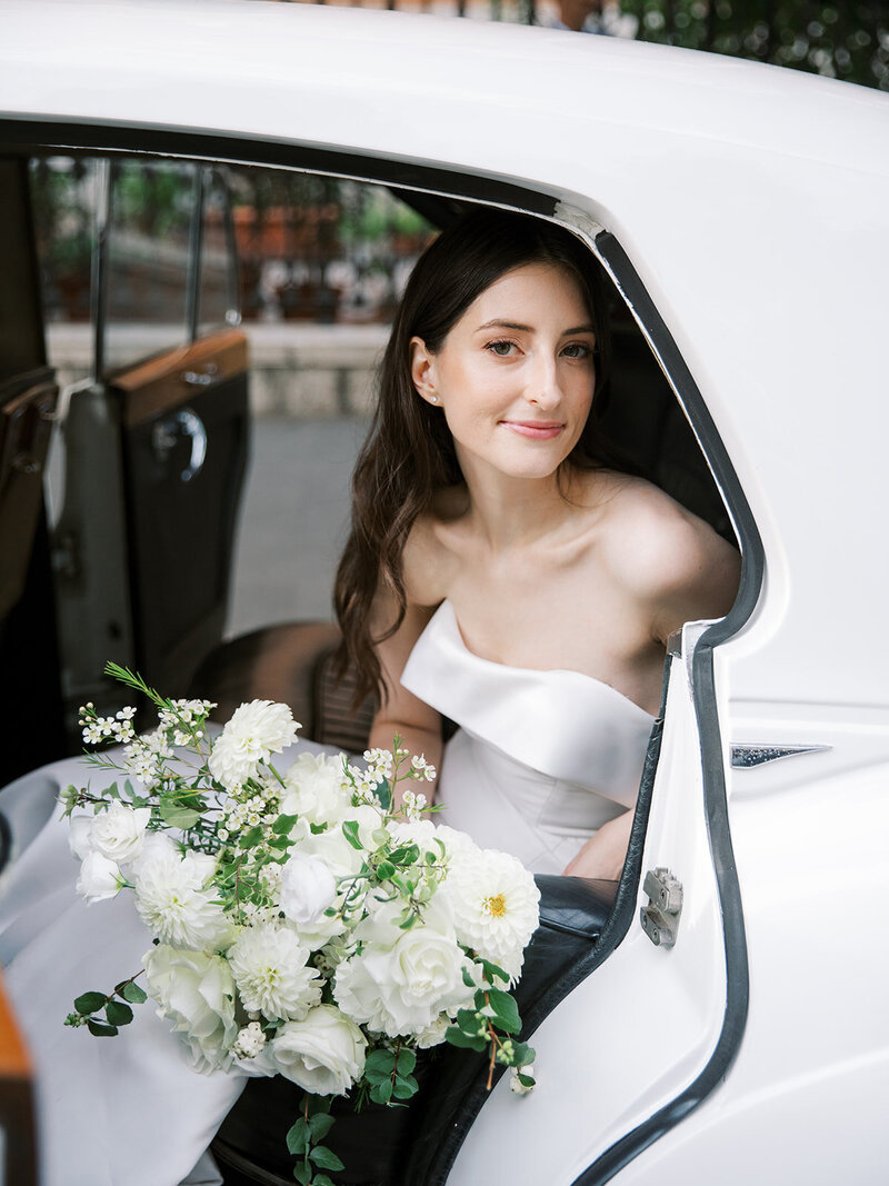 Bride in the getaway car on the way to church. She is looking at the camera with her flowers in her lap.