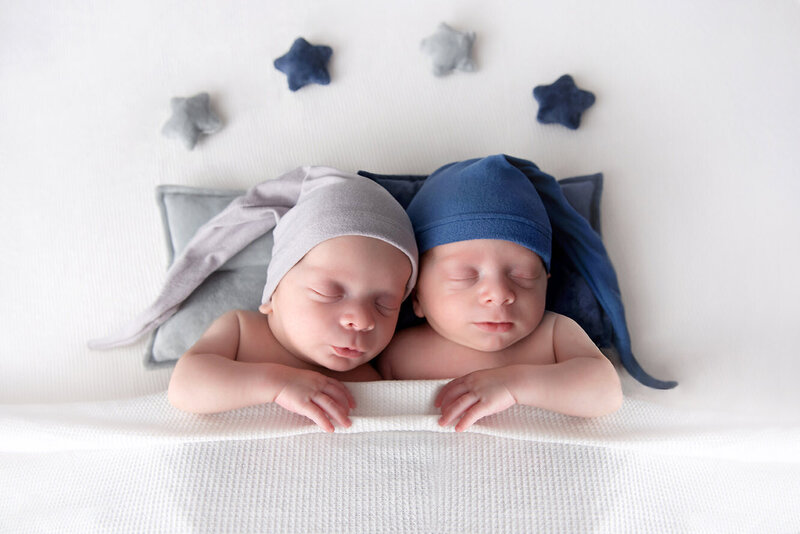 Newborn twin boys snuggling up together with matching sleepy caps.