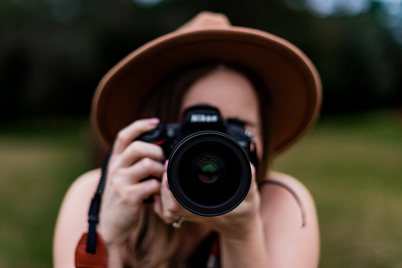 Women in brown hat holding up camera as if she is going to take a photograph