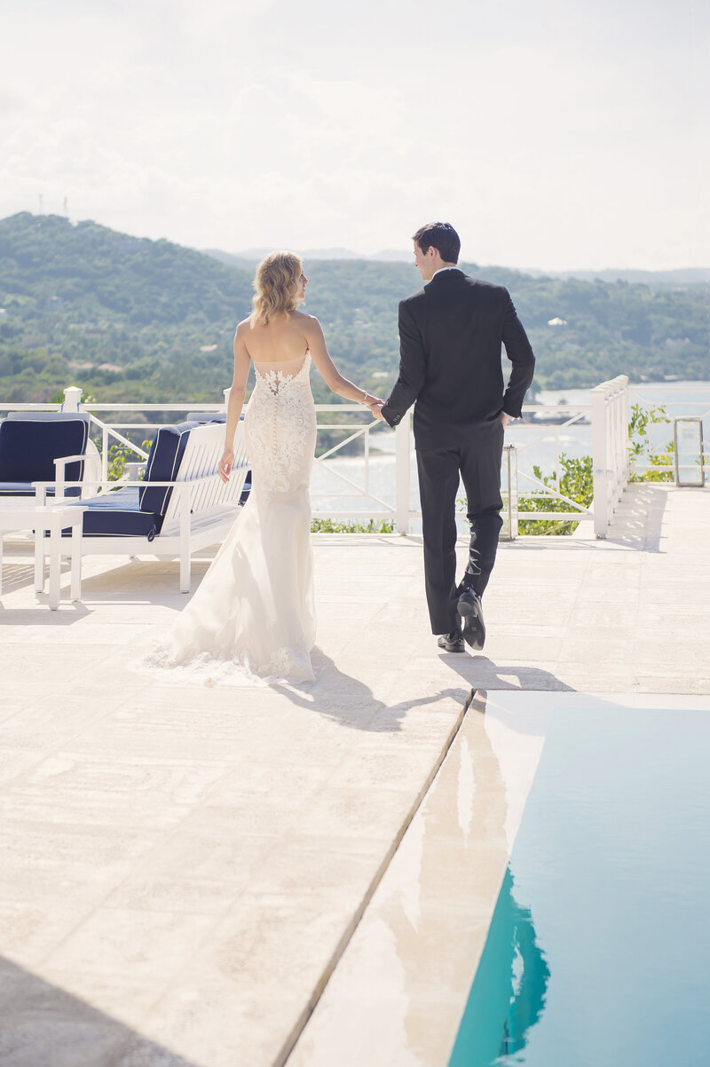 Bride and groom holding hands walking next to pool