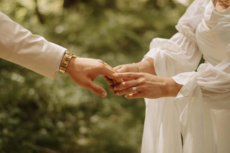 Close up shot of a bride holding the grooms hand with greenery in the background