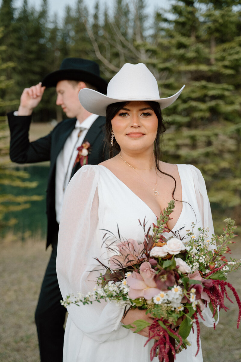 Groom stands behind bride as she poses for a solo photo outside in Banff