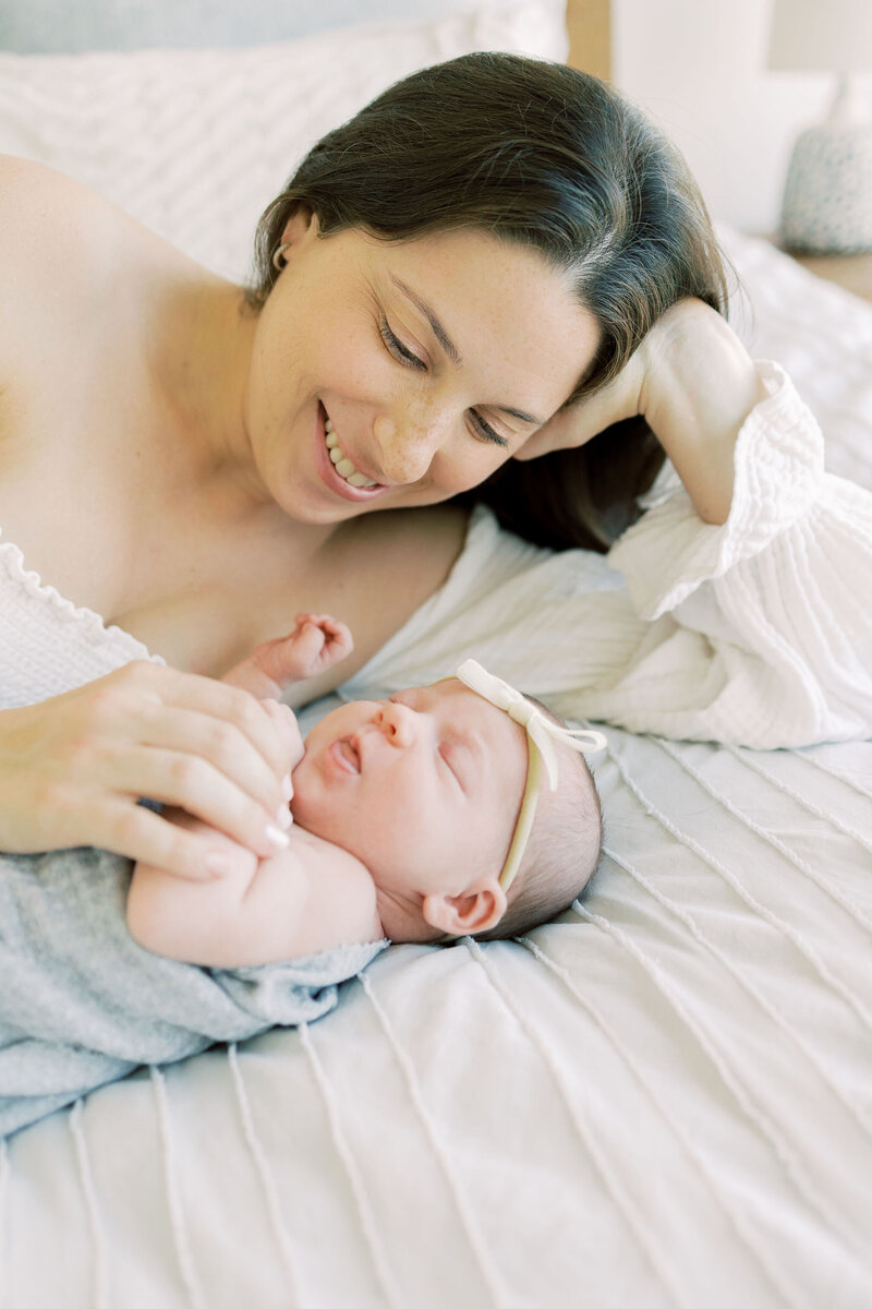 Mom admires baby on bed during newborn session.
