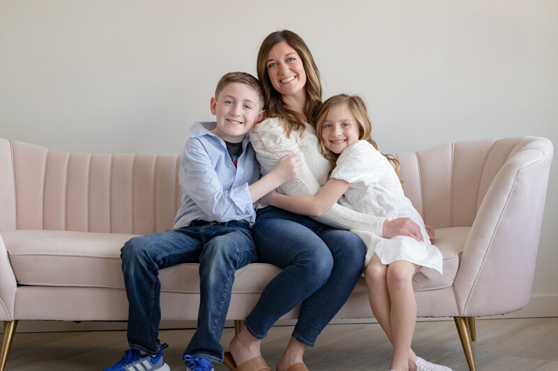 A mom with her two kids smiling on a couch.