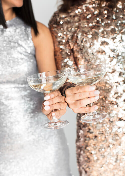 Close up of two women in sequined dresses clinking champagne glasses