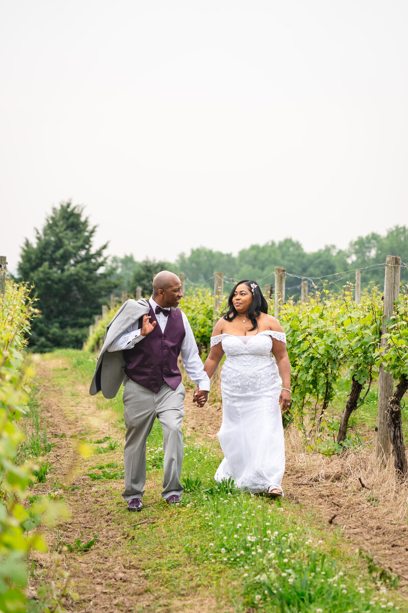 Elegant bride and groom holding hands while strolling through vineyard, photographed by wedding photographer Niko Coric - Lumen Clarity Media