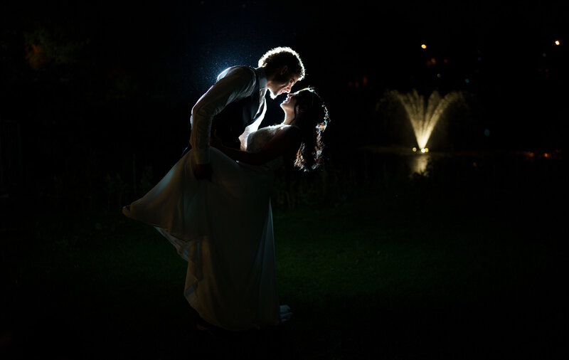 Bride and groom sharing a romantic backlit night-time dip with glowing silhouettes and a lit fountain behind them during their Denver wedding.