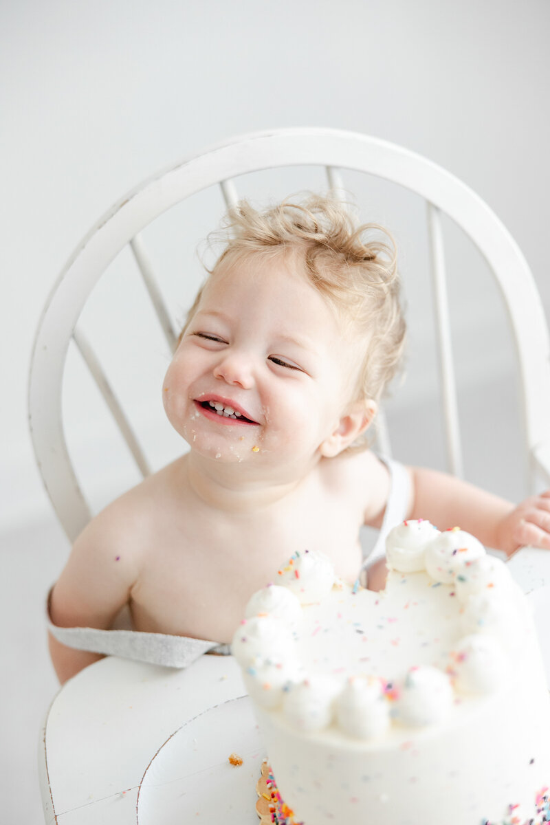 One year old baby boy smiles joyfully during cake smash portrait session