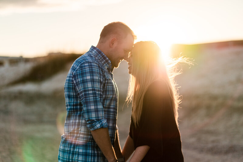 Couple with foreheads together with sun setting behind them at beach in Tybee Island, GA. Engagement photos.