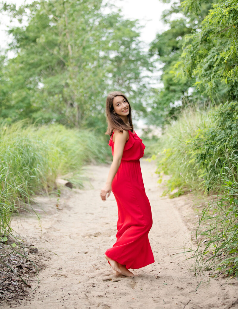 Senior portrait of a girl in a red dress twirling at Presque Isle State Park in Erie Pa