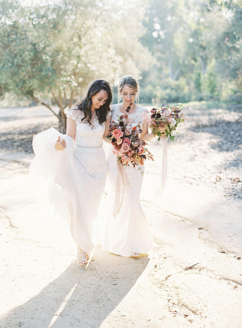 Two brides walk in the sunlight near olive grove at Rancho Valencia wedding with San Diego wedding photographer Jacqueline Benet Photography