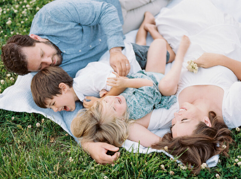A family lays down on a blanket laughing during their family photo session by Northern VA Family Photographer Marie Elizabeth Photography