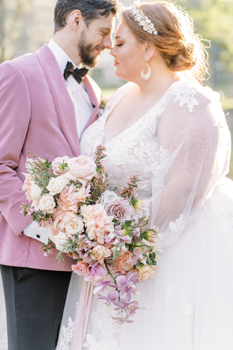 A bride and groom touching foreheads and holding hands behind the bridal bouquet at their Villa Montalvo Wedding.