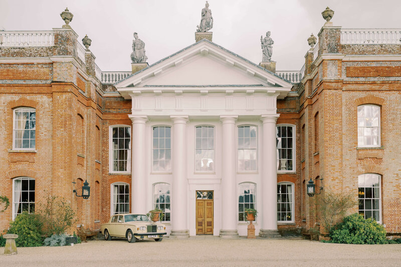 front facade of luxury wedding venue avington park house with a vintage rolls royce car parked in front of it